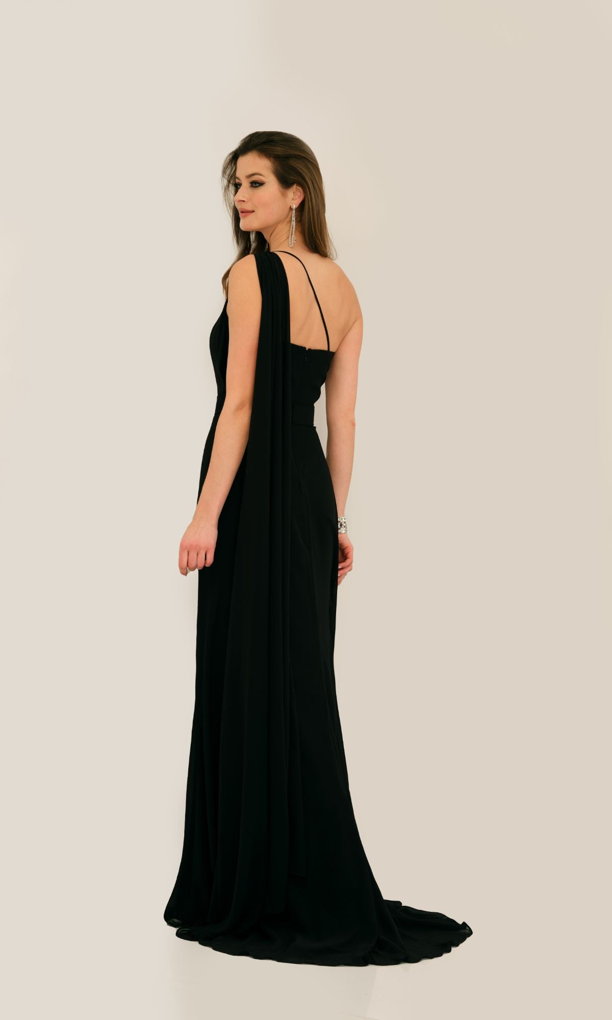 A woman in the Caped Strapless Long Prom Dress by Dave & Johnny 11288 stands against a plain background, her elegant black A-line gown flowing gracefully as she looks to the side.